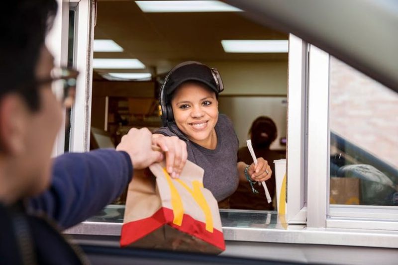 A McDonald&rsquo;s crew member handing an order through the drive-thru window